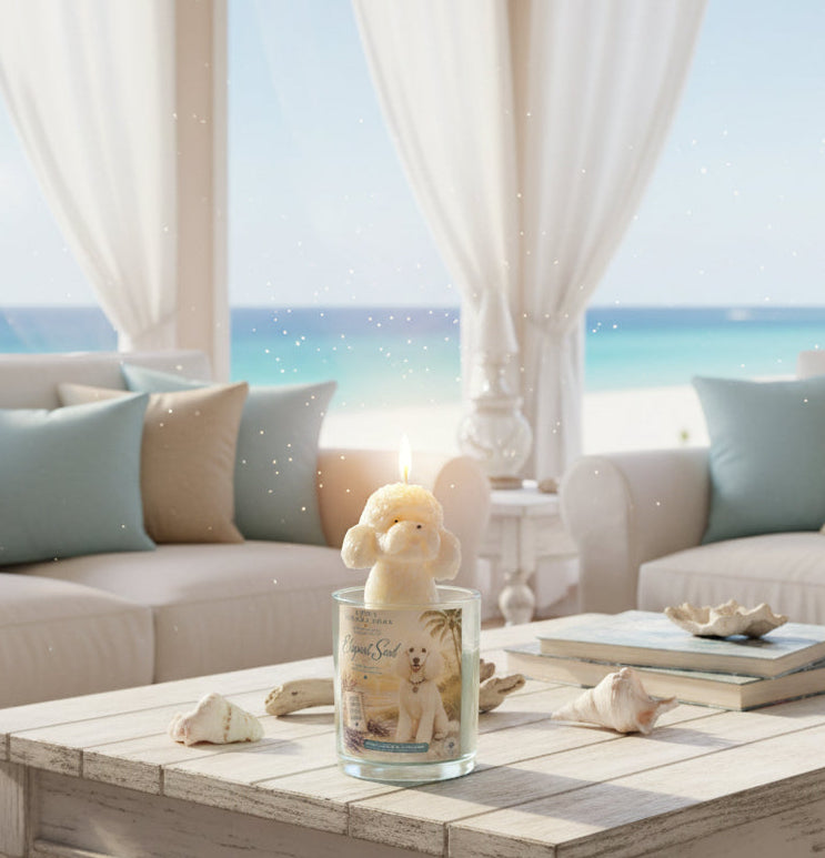 Hand-poured coconut wax poodle candle with a sculpted white poodle wax topper and Elegant Soul label, displayed on a rustic coffee table with seashells in a bright coastal living room overlooking the ocean.