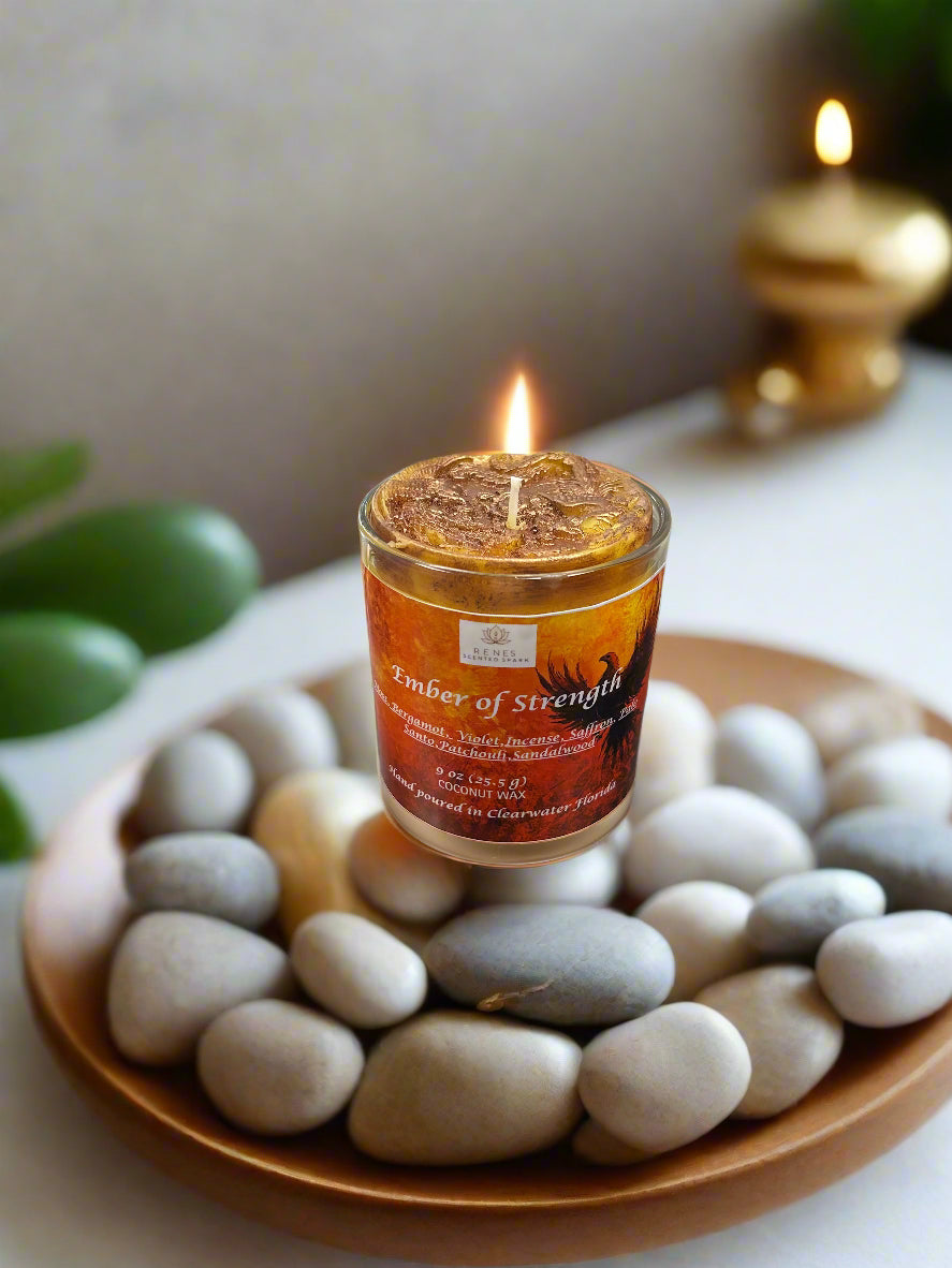 Spiritual candle collection displayed on a wooden table with Ember of Strength candle topped with phoenix and dragon, and Tranquil Spirit candle beside a Buddha figure. Surrounded by crystals, stones, and greenery — symbolic gift candles for meditation, healing, and renewal