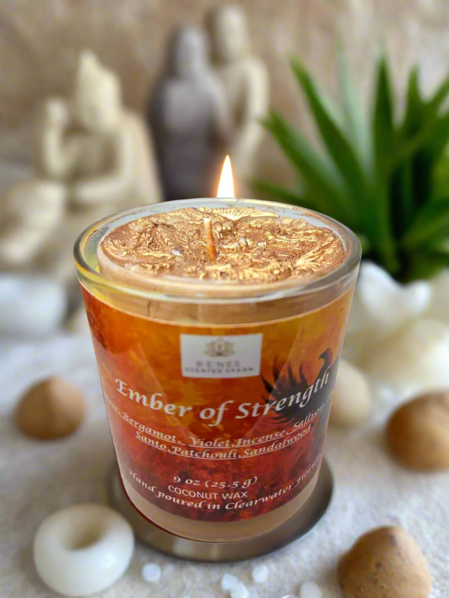 Spiritual candle collection displayed on a wooden table with Ember of Strength candle topped with phoenix and dragon, and Tranquil Spirit candle beside a Buddha figure. Surrounded by crystals, stones, and greenery — symbolic gift candles for meditation, healing, and renewal