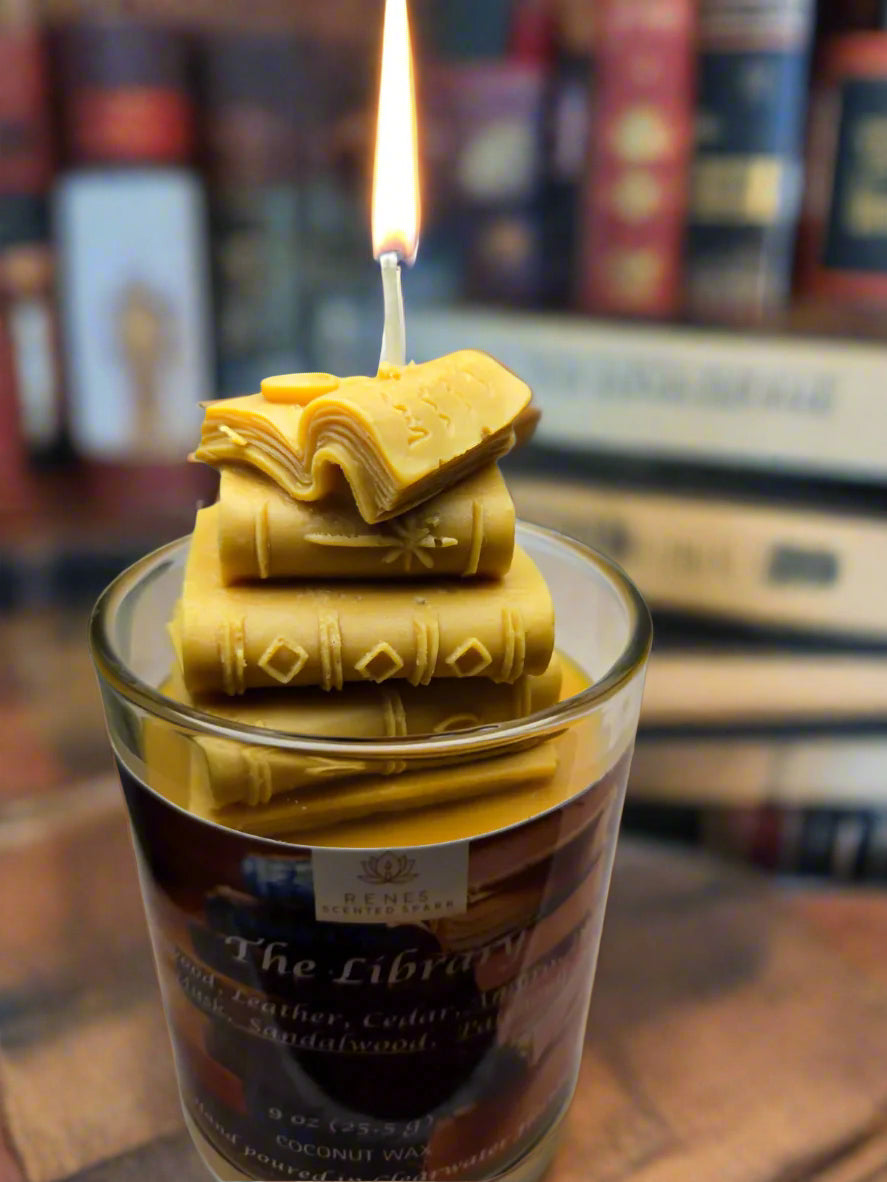 The Library candle with stacked book wax embed, hand-poured coconut wax with teakwood, cedar, leather, sandalwood, patchouli, and dark musk fragrance — perfect gift for book lovers