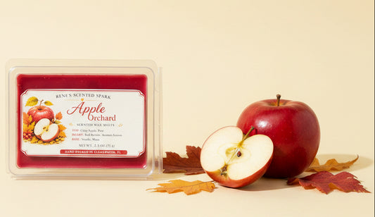 Apple Orchard 2.5 oz scented wax melts displayed with a fresh red apple, sliced apple and colorful autumn leaves on a warm cream background.