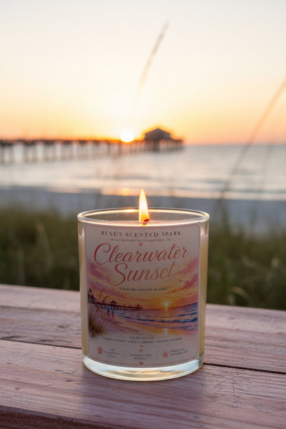 Lit Clearwater Sunset hand-poured coconut wax candle displayed on a wooden table overlooking Clearwater Beach at sunset. Coastal-inspired candle with a vibrant Florida sunset label by Rene's Scented Spark.