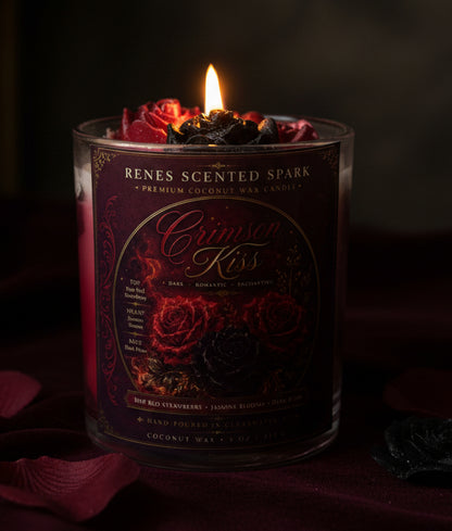 Crimson Kiss coconut wax candle glowing in a dark romantic setting with crimson and black rose wax toppers, burgundy velvet, and scattered rose petals.