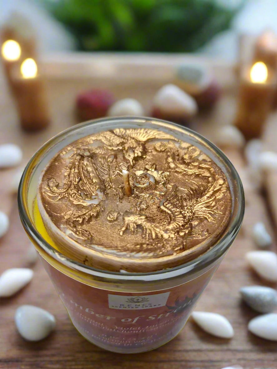 Spiritual candle collection displayed on a wooden table with Ember of Strength candle topped with phoenix and dragon, and Tranquil Spirit candle beside a Buddha figure. Surrounded by crystals, stones, and greenery — symbolic gift candles for meditation, healing, and renewal