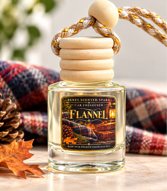 A car fragrance bottle labeled 'Flannel' by Renes Scented Spark, filled with pale yellow liquid and topped with a light wood cap and braided cord, set on a tabletop with a plaid blanket, pinecone, and autumn leaf in the background.