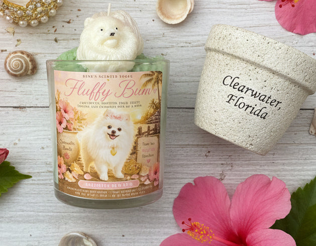 Candle with a dog design label on a wooden surface with flowers and a container.