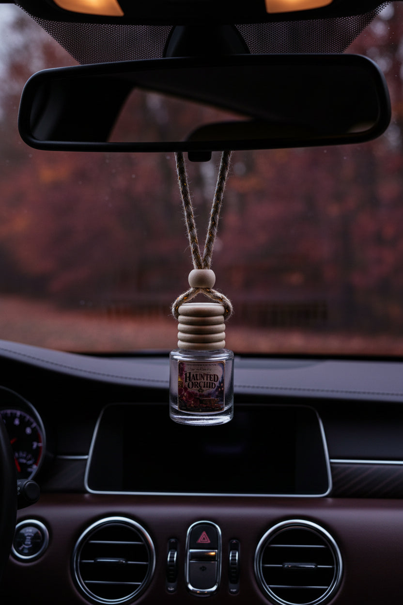 Haunted Orchid hanging car air freshener suspended from a rearview mirror inside a dark, elegant car interior, with moody autumn scenery visible through the windshield.