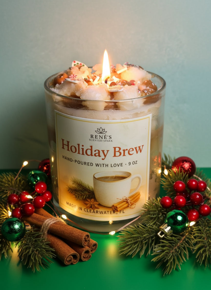Lit candle in a glass jar labeled 'Holiday Brew' with festive decorations on a green surface.
