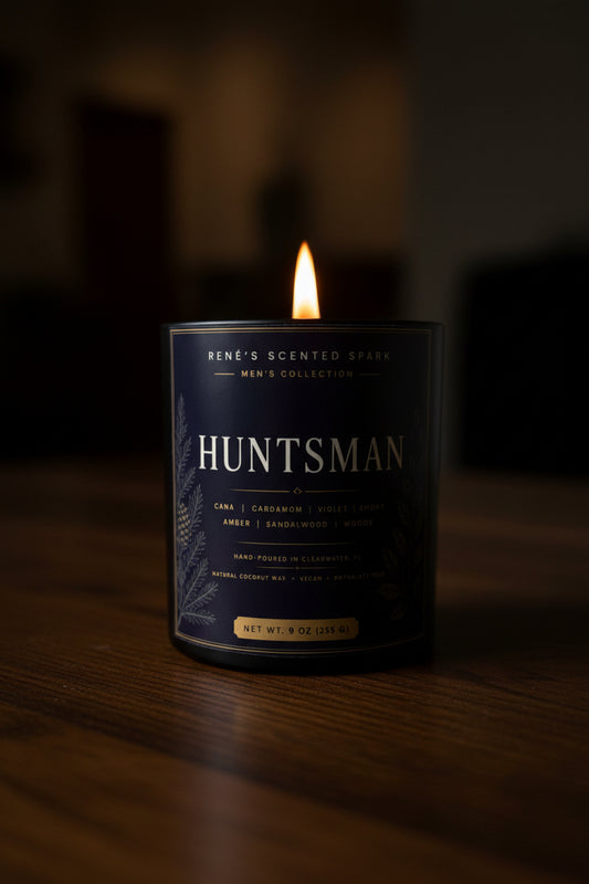 Candle labeled 'Huntsman' with a dark label and visible flame on a wooden surface.