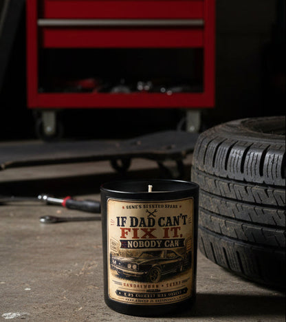 If Dad Can't Fix It Nobody Can candle displayed in a garage next to a classic car tire and red toolbox