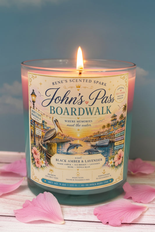 Candle with 'John's Pass Boardwalk' label on a wooden surface with pink petals