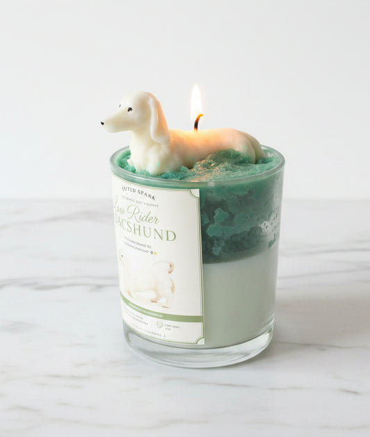 Low Rider Dachshund candle with lit cream dog wax topper on teal green whipped wax on white marble surface
