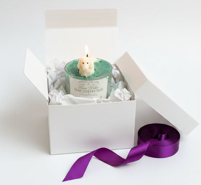 Low Rider Dachshund candle in open white gift box with purple ribbon on clean white background luxury gift presentation