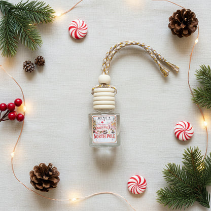 North Pole peppermint and vanilla car freshener by Rene’s Scented Spark styled with peppermint candies, evergreen branches, pinecones, red berries, and warm Christmas lights