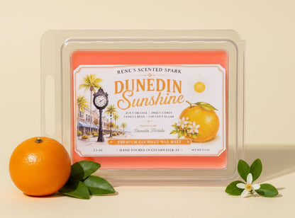 Dunedin Sunshine orange citrus wax melts by Rene’s Scented Spark displayed with a fresh orange, green leaves, and delicate orange blossoms on a warm cream background.