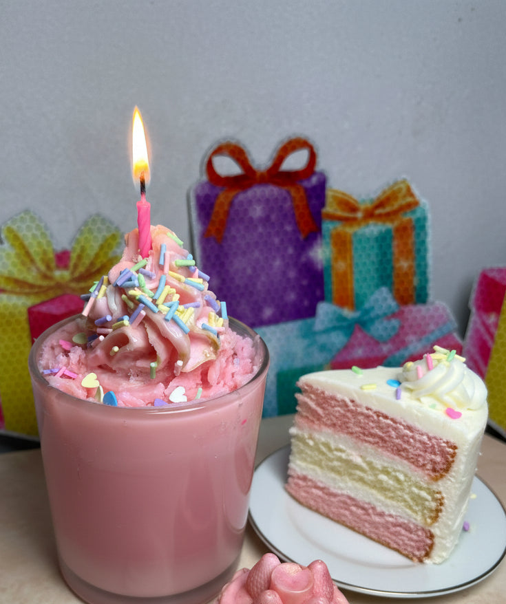 Happy Birthday candle made with coconut wax, topped with pink swirl and colorful sprinkles with a slice of cake