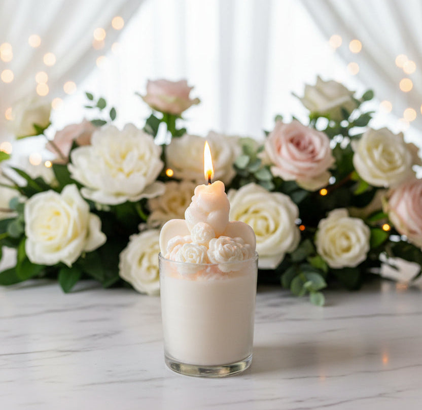 Bride and groom candle in glass jar with sculpted roses, glowing flame, white roses, and soft warm lights in background