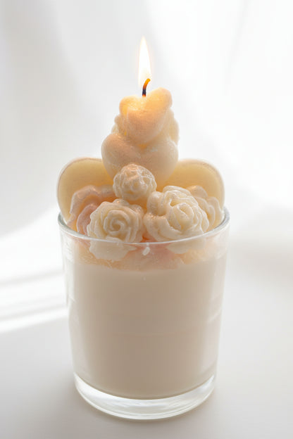 Bride and groom candle in glass jar with sculpted roses, glowing flame, white roses, and soft warm lights in background