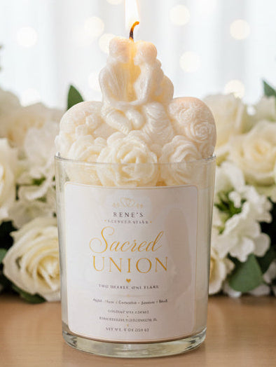 Bride and groom candle in glass jar with sculpted roses, glowing flame, white roses, and soft warm lights in background