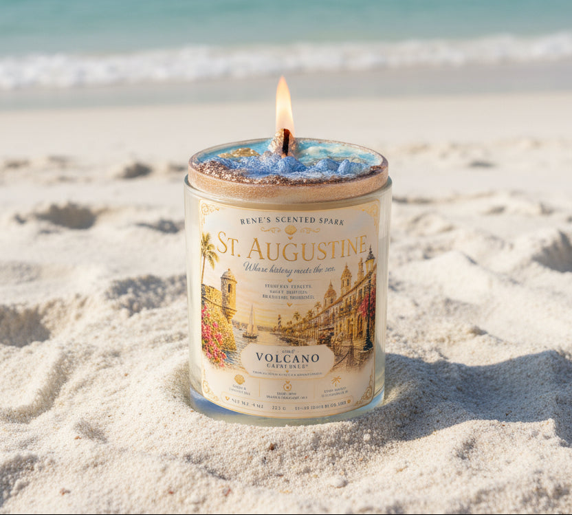 Lit St. Augustine coconut wax candle by Rene's Scented Spark displayed on white Florida beach sand, featuring a vintage-inspired city label and handcrafted ocean-inspired blue wax.