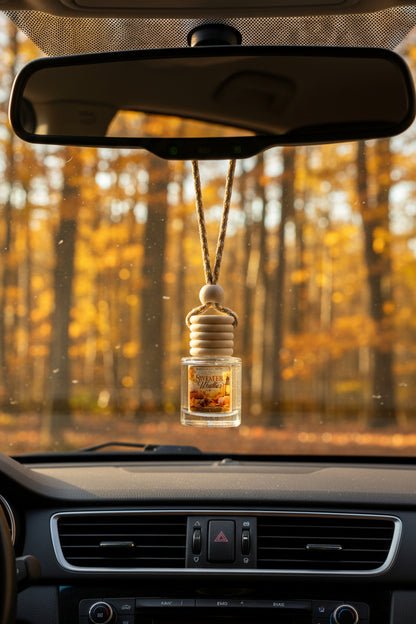 Sweater Weather hanging car freshener by Rene’s Scented Spark displayed from a rearview mirror with golden autumn trees and warm fall sunlight in the background.