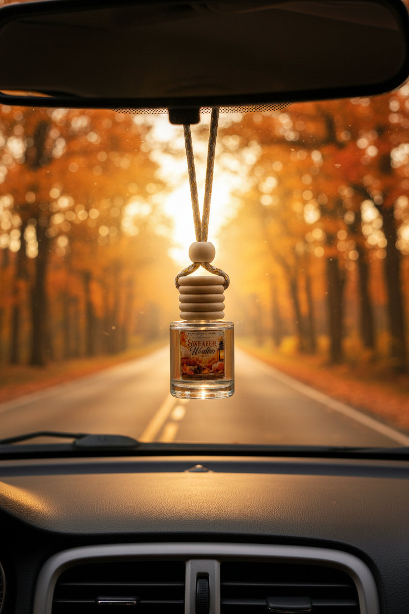 Sweater Weather hanging car freshener by Rene’s Scented Spark displayed from a rearview mirror on a scenic autumn road surrounded by glowing orange and golden fall trees