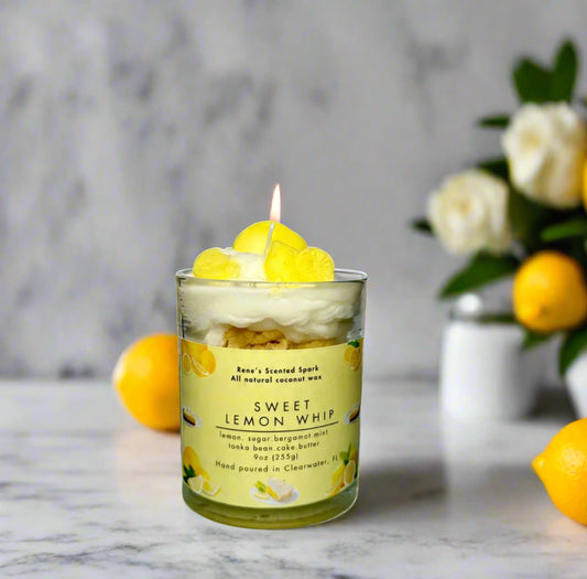 Sweet Lemon Whip candle glowing on a kitchen counter beside lemons, a slice of cake, and fresh flowers — citrus dessert candle perfect for gifting
