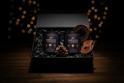 Two cans of 'Tobacco Vanille' in a decorative box with pine cones and a small bag on a wooden surface.