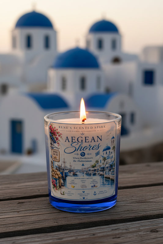Aegean Shores candle glowing on a wooden surface with stunning white and blue domed Santorini architecture in the background at dusk