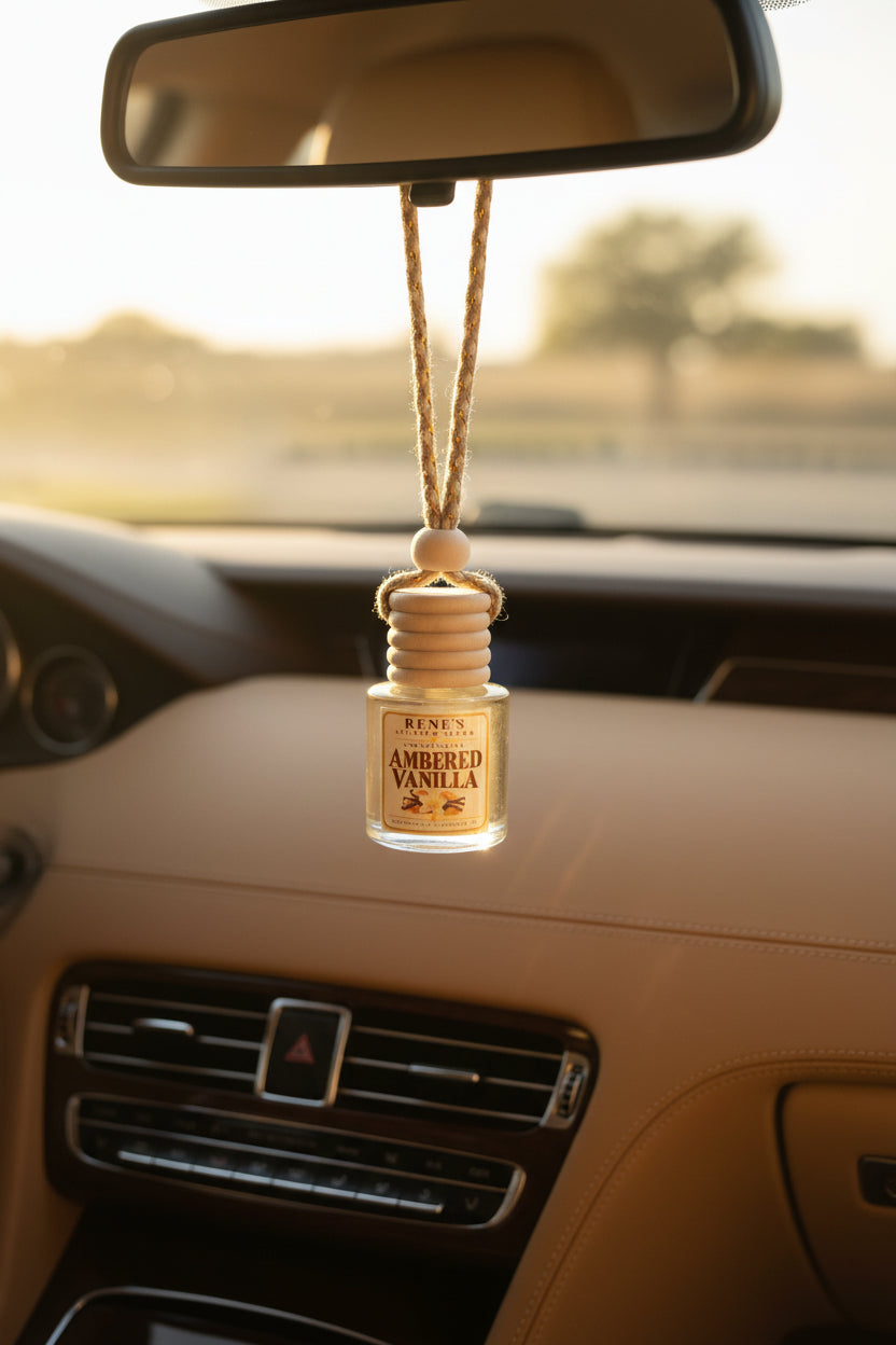 Ambered Vanilla hanging car freshener by Rene’s Scented Spark displayed from a rearview mirror in a tan leather car interior with warm golden sunlight