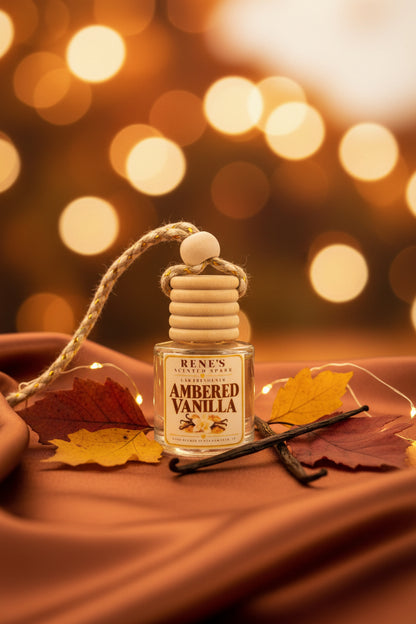 Ambered Vanilla car freshener by Rene’s Scented Spark styled with autumn leaves, vanilla beans, warm golden lights, and rich brown fabric for a cozy fall setting.