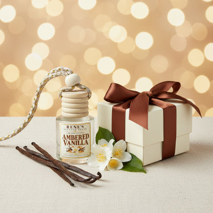 Ambered Vanilla car freshener by Rene’s Scented Spark styled beside a cream gift box with a brown satin bow, vanilla beans, and white flowers against a warm golden background.