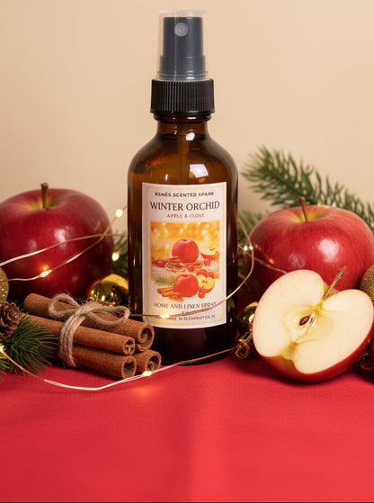 Bottle of 'Winter Orchard' scented spray with apples and cinnamon sticks on a red surface