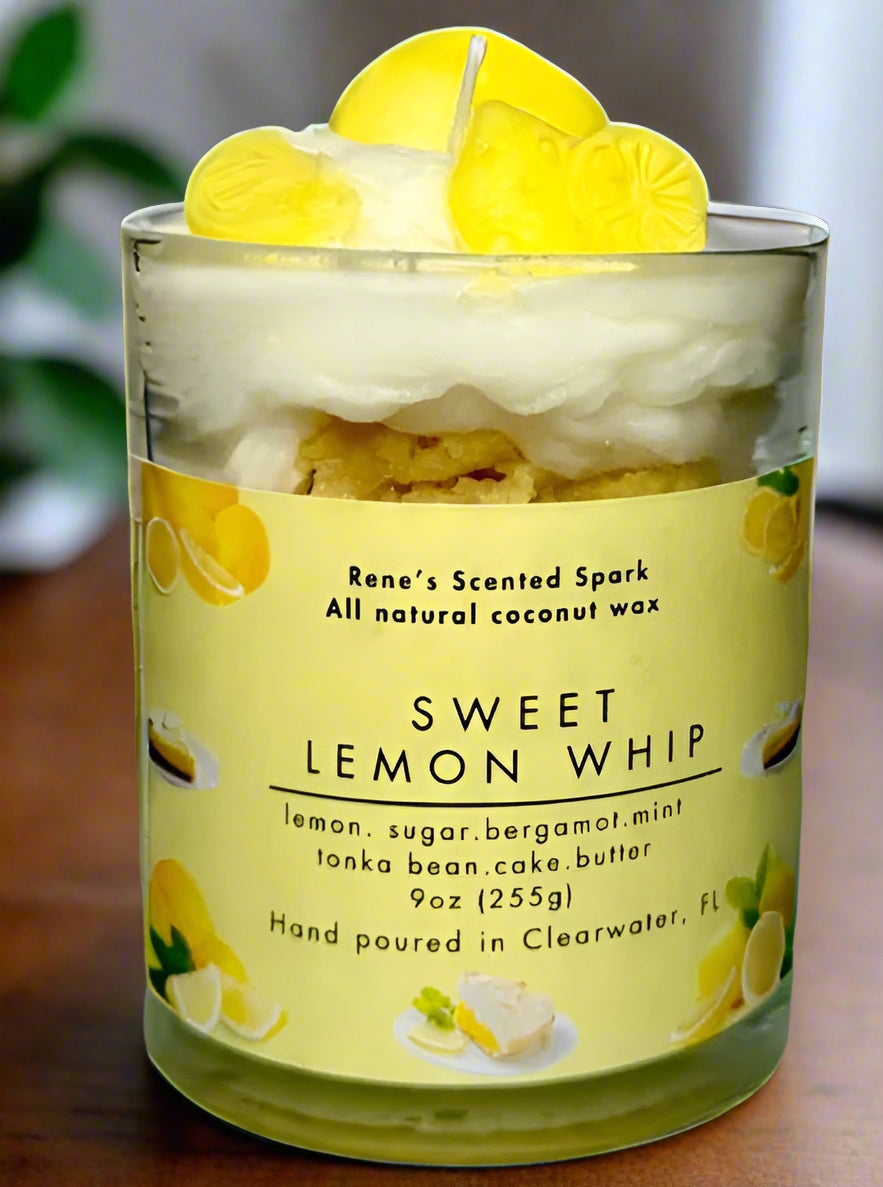 Sweet Lemon Whip candle glowing on a kitchen counter beside lemons, a slice of cake, and fresh flowers — citrus dessert candle perfect for gifting.