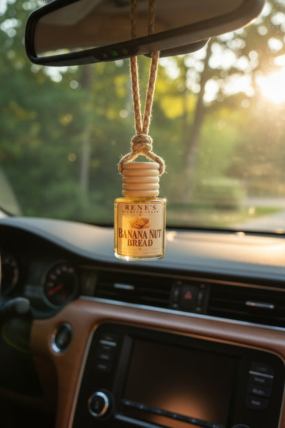 Banana Nut Bread hanging car air freshener by Rene’s Scented Spark suspended from a rearview mirror inside a car with warm golden sunlight and greenery outside.