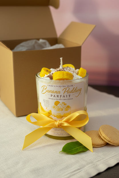 Banana pudding-themed candle with a yellow bow in front of an open box.