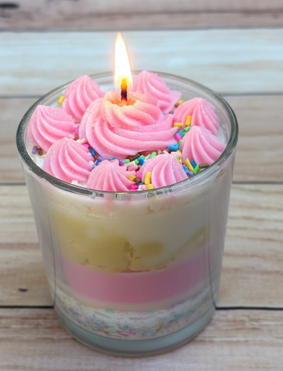 Candle with pink frosting and sprinkles on a wooden surface