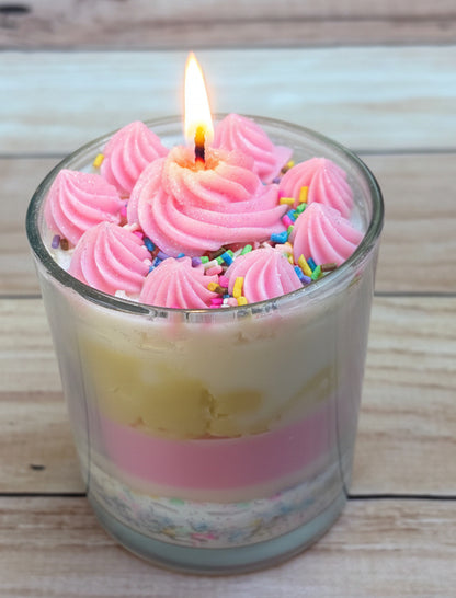 Candle with pink frosting and sprinkles on a wooden surface