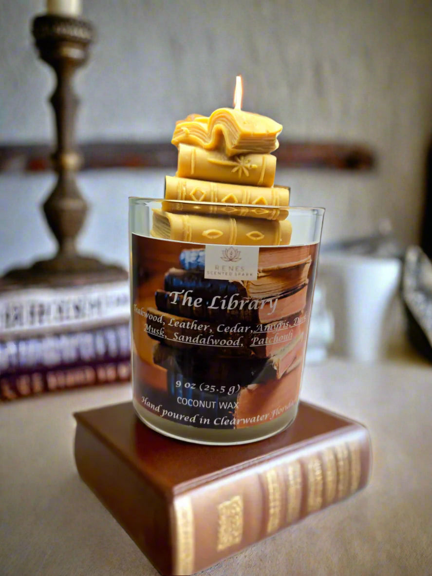 The Library candle with stacked book wax embed, hand-poured coconut wax with teakwood, cedar, leather, sandalwood, patchouli, and dark musk fragrance — perfect gift for book lovers