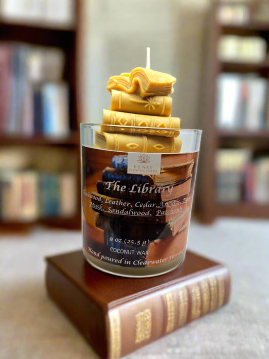 The Library candle with stacked book wax embed, hand-poured coconut wax with teakwood, cedar, leather, sandalwood, patchouli, and dark musk fragrance — perfect gift for book lovers