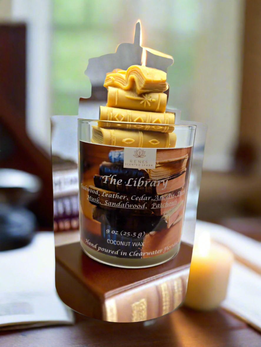 Library candle glowing beside leather-bound books and mahogany shelves, evoking a refined old-world reading atmosphere — perfect gift for readersThe Library candle with stacked book wax embed, hand-poured coconut wax with teakwood, cedar, leather, sandalwood, patchouli, and dark musk fragrance — perfect gift for book lovers