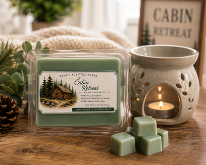 Cabin Retreat scented wax melts by Renes Scented Spark beside a glowing wax warmer, styled with green wax cubes, pinecones and greenery in a cozy rustic cabin setting.