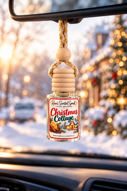 Christmas Cottage car freshener hanging from a rearview mirror with a snowy street and Christmas lights outside