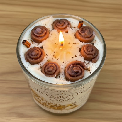 Candle labeled 'Cinnamon Roll Bliss' by Rene's Scented Spark on a wooden surface.