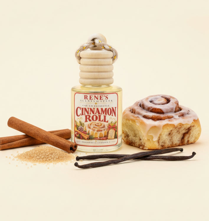 Cinnamon Roll hanging car air freshener by Rene’s Scented Spark displayed beside a frosted cinnamon roll with cinnamon sticks, brown sugar, and vanilla beans on a clean cream background. 🤎