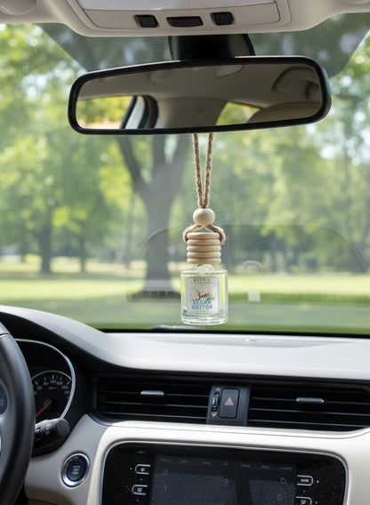 Clean Cotton hanging car air freshener by Rene’s Scented Spark suspended from a rearview mirror inside a clean car with a sunny green outdoor view through the windshield.