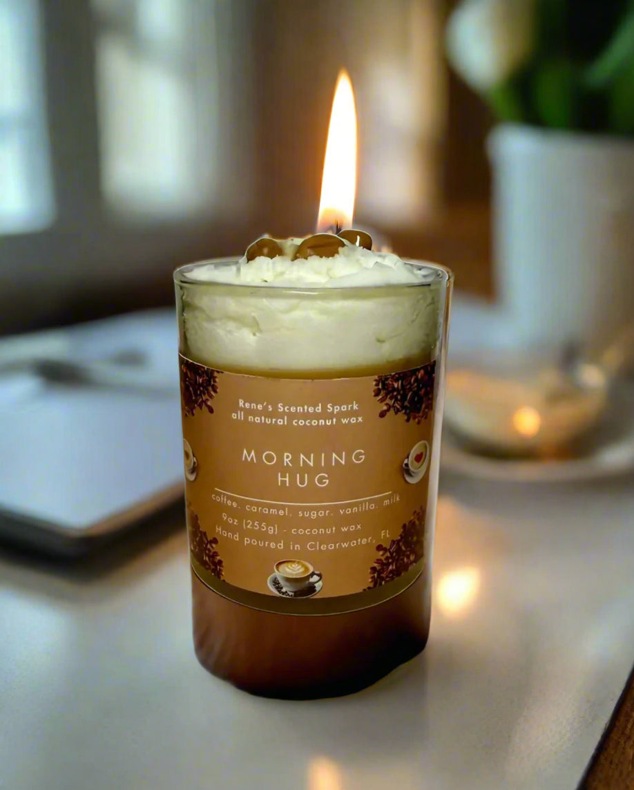 Morning Hug candle glowing beside a steaming coffee mug, books, and cozy blanket — coffee and caramel candle perfect for gifting