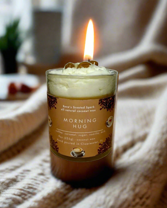 Morning Hug candle glowing beside a steaming coffee mug, books, and cozy blanket — coffee and caramel candle perfect for gifting