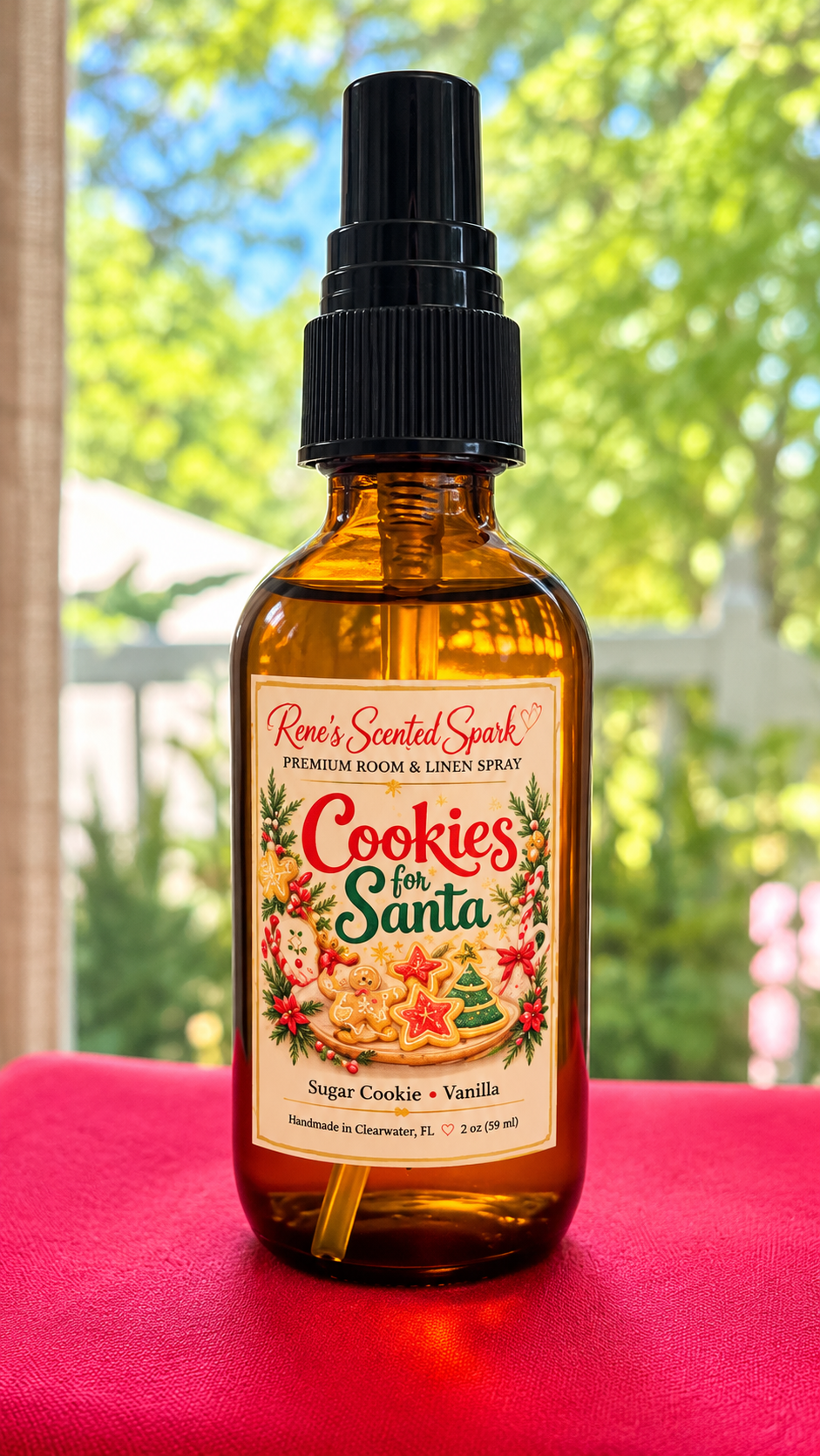 Rene's Scented Spark Cookies for Santa 2 oz room spray in amber glass bottle with sugar cookie label on red fabric outdoors