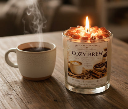 Lit Cozy Brew coconut wax candle by Rene's Scented Spark with a coffee bean wax topper, displayed beside a steaming cup of coffee on a rustic wooden table.